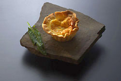 Mini-Quiche auf einem Schieferbrocken mit kleinem Spinatblatt, dunkelblauer Hintergrund